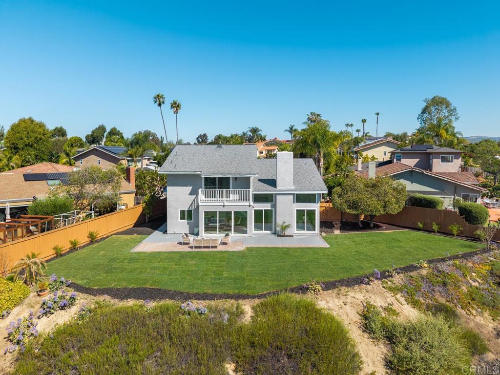 Two-story gray home with a balcony overlooking a broad backyard lawn and patio.