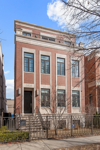 Red-brick multi-story residence with tall windows, front steps, and a metal fence.