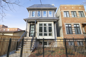 Multi-story gray home with large windows and a black metal front fence.
