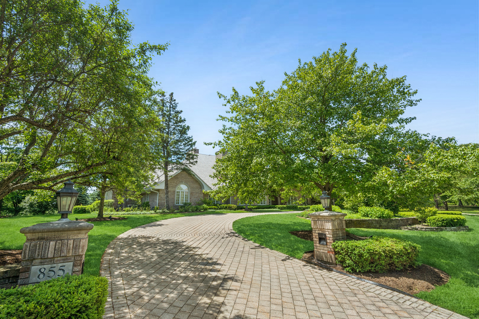 855 Jennifer Court home behind a curved paver driveway, framed by mature trees and landscaped lawns.