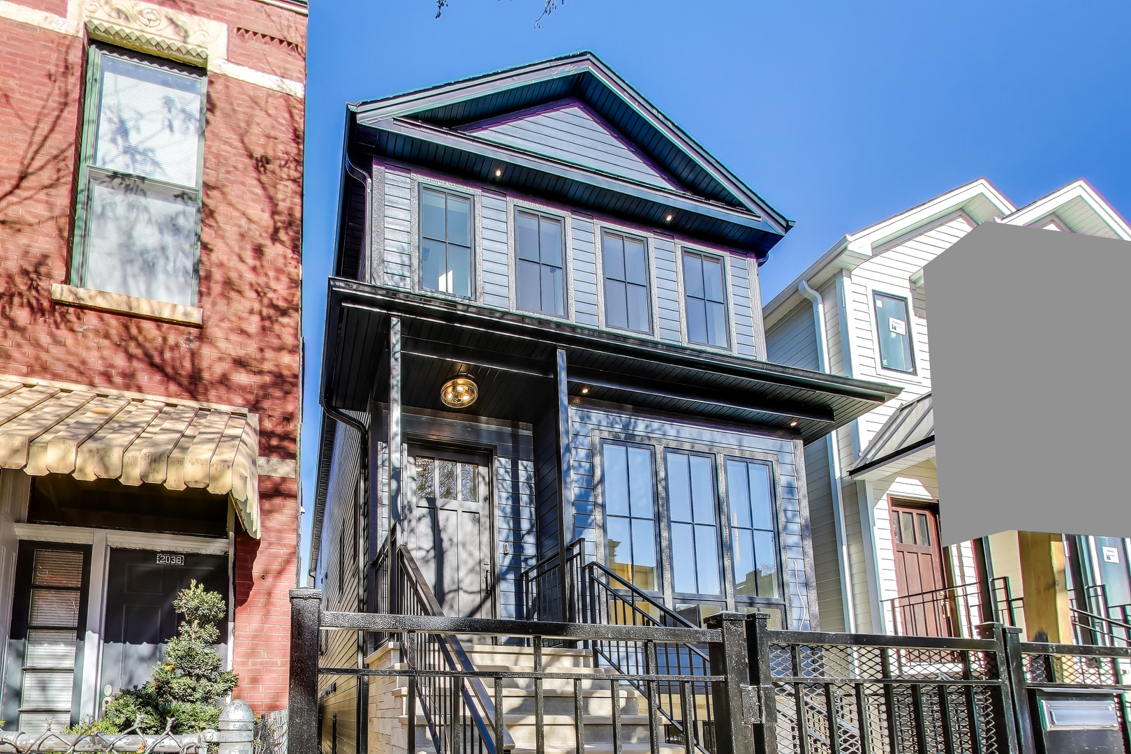Dark gray two-story house with a gabled roof, tall windows, and a black metal front fence.