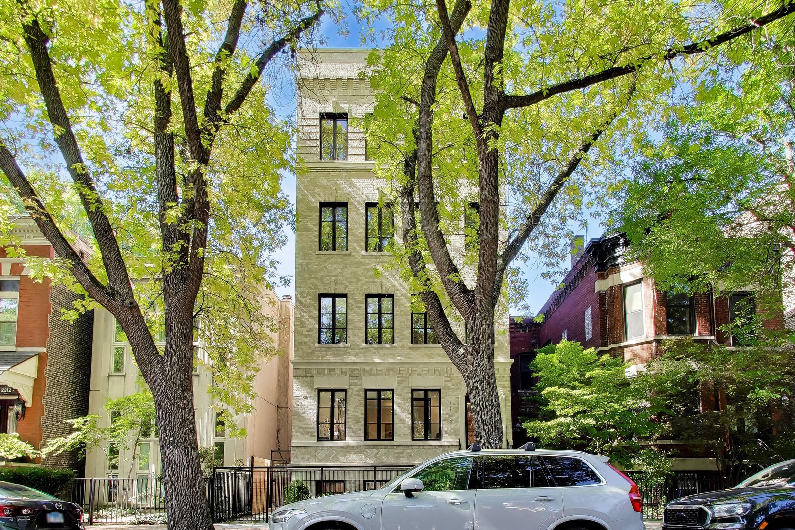 Light brick residence with black-framed windows, framed by mature trees along a city street.