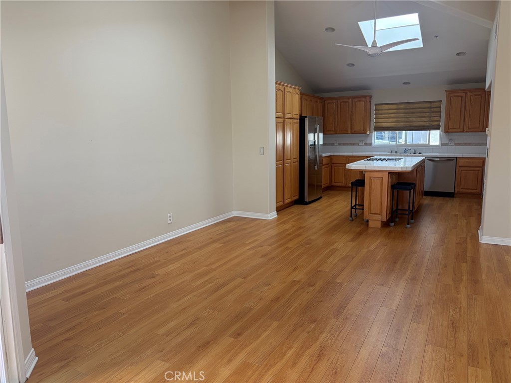 Empty dining area opening to a wood-cabinet kitchen with an island, hardwood floors, and skylight.