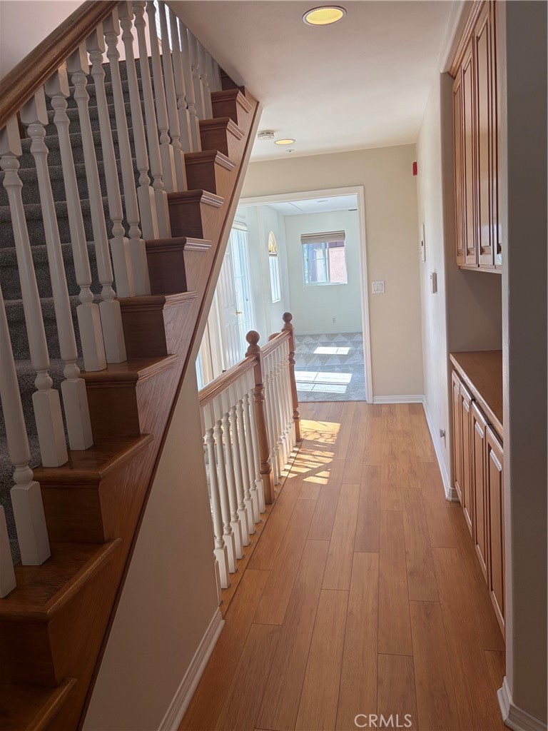 Hallway with a wood staircase, white balusters, built-in cabinets, and sunlight on the wood floor.