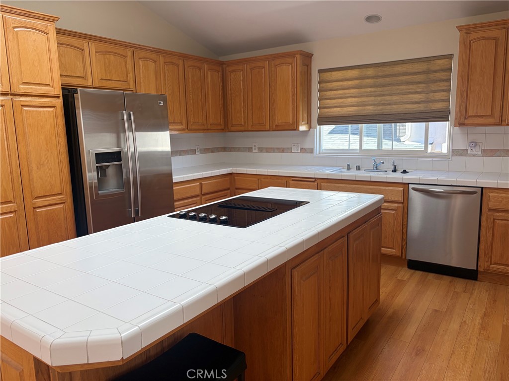 Kitchen with a large white-tile island cooktop, honey-toned cabinets, and stainless steel appliances.