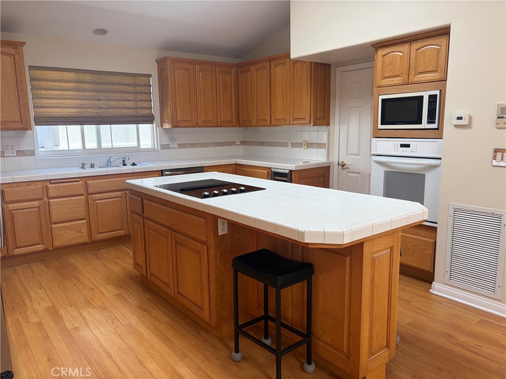Kitchen with wood cabinetry, a large cooktop island, white tile counters, and wood flooring.