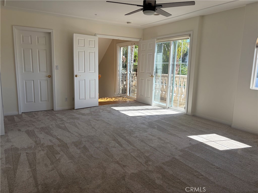 Empty carpeted room with a ceiling fan and sliding glass doors opening to a balcony.
