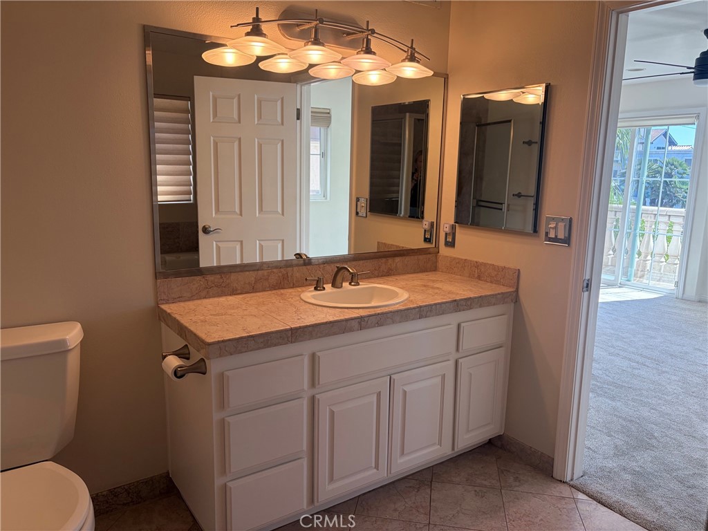 Bathroom vanity with a pink marble countertop, large mirror, and warm multi-light fixture.