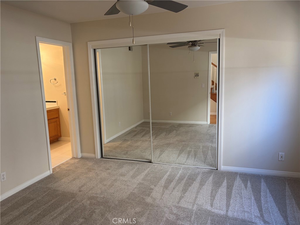 Empty carpeted bedroom with mirrored closet doors, a ceiling fan, and a bathroom doorway.