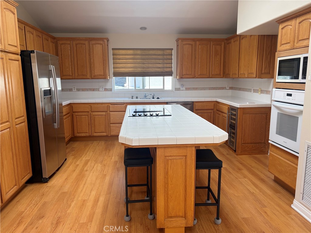 Kitchen with a large tiled island, wood cabinetry, stainless steel refrigerator, and built-in oven.