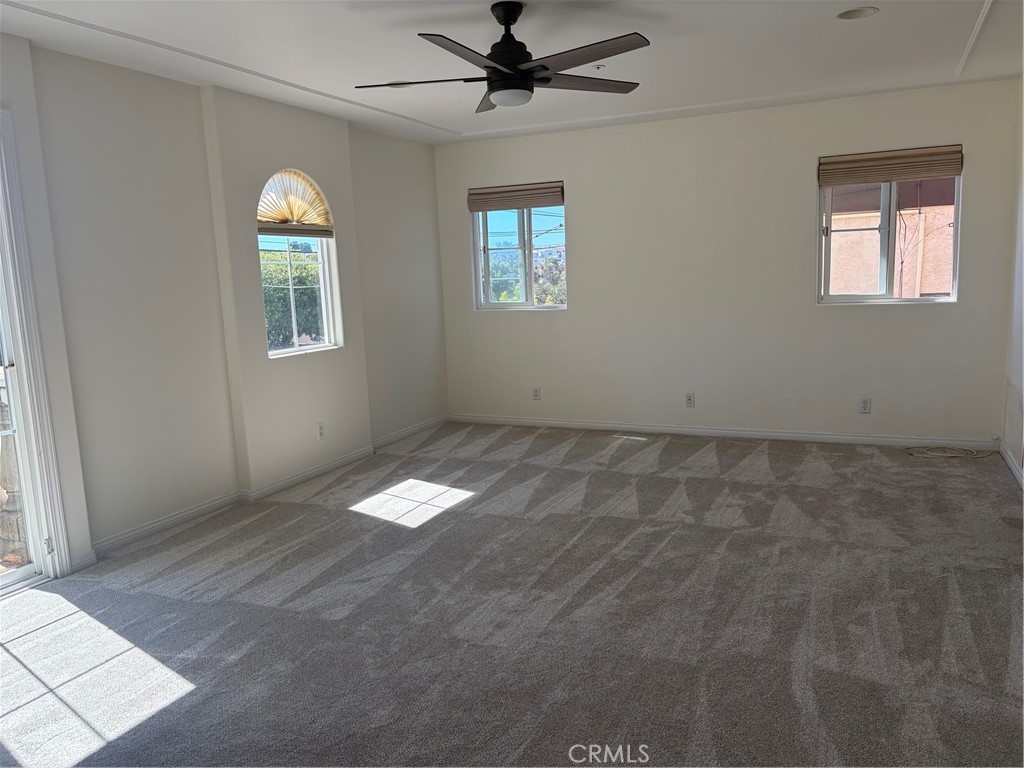 Empty carpeted room with a ceiling fan, three windows, and a sliding glass door.