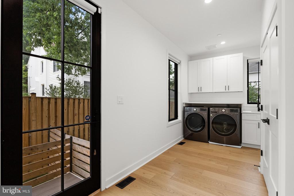 Laundry room with side-by-side front-loading washer and dryer, white cabinets, and a glass door to a fenced yard.