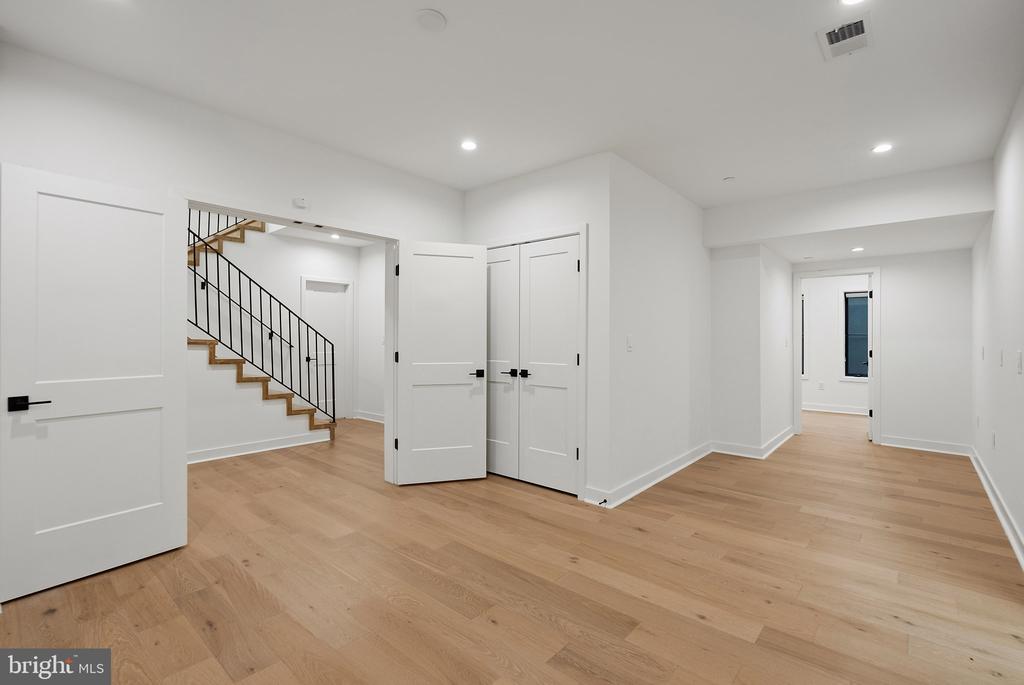 Empty foyer with light wood floors and a staircase with black metal railing.