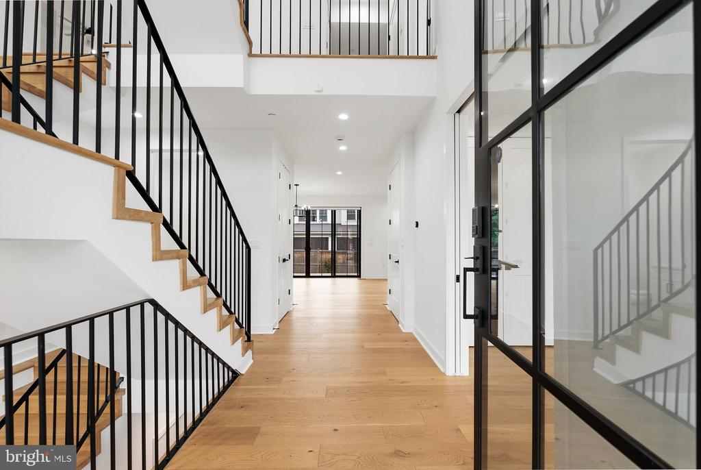Entry hall with pale wood floors, a black metal staircase, and a glass front door.