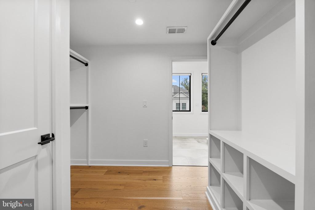 Walk-in closet with white built-in shelves, hanging rods, and hardwood flooring.