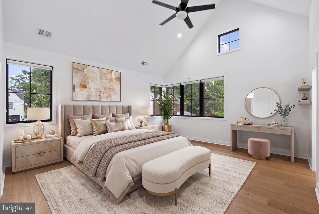 Staged bedroom with a king bed, curved bench, vaulted ceiling, and large black-framed windows.
