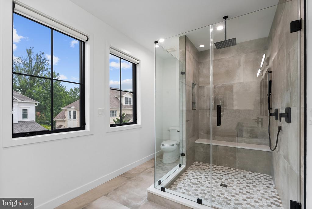 Modern bathroom with a glass walk-in shower, hexagonal tile floor, and two large windows.
