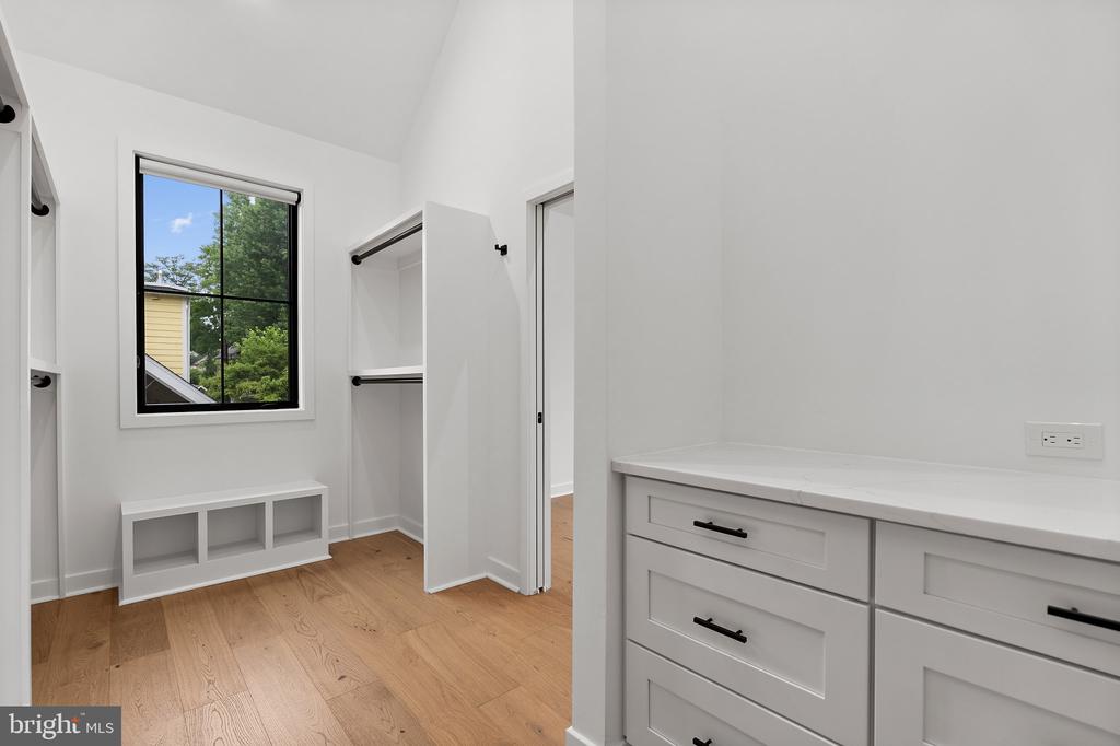 Walk-in closet with built-in white drawers, open shelving, and a black-framed window.