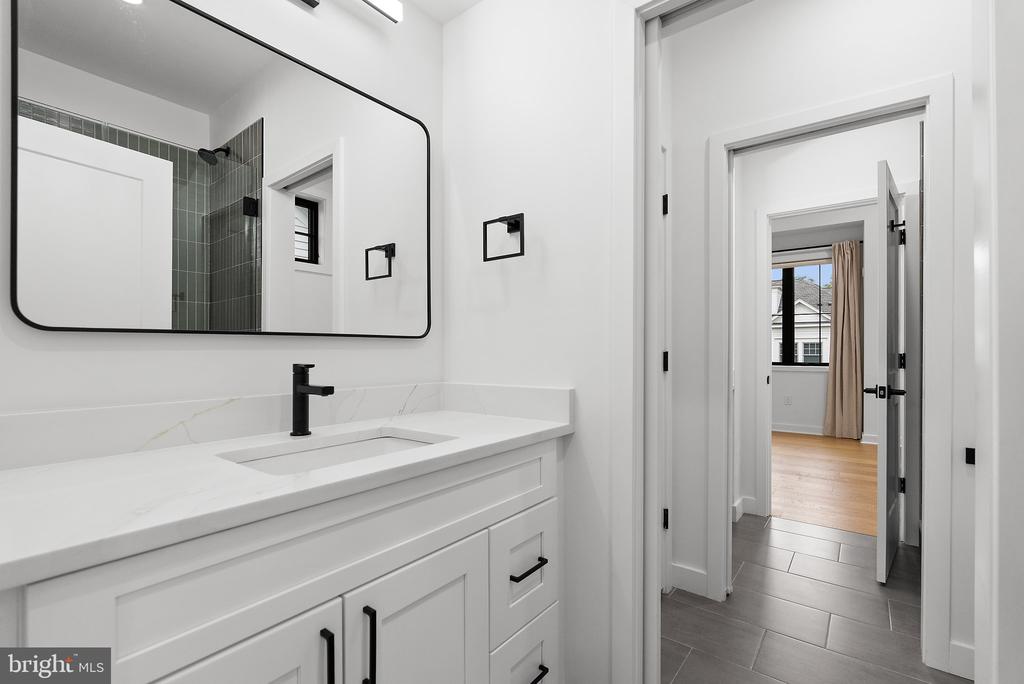 Bright bathroom with a white vanity, black fixtures, and a large mirror reflecting a tiled shower.
