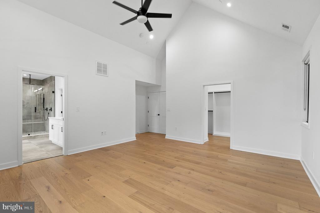 Vacant bedroom with vaulted ceiling, hardwood floors, ceiling fan, open closet, and adjoining bathroom.