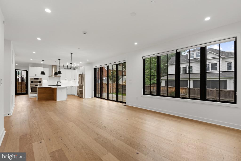 Open-plan kitchen and living area with a wood-front island, hardwood floors, and large black-framed windows.