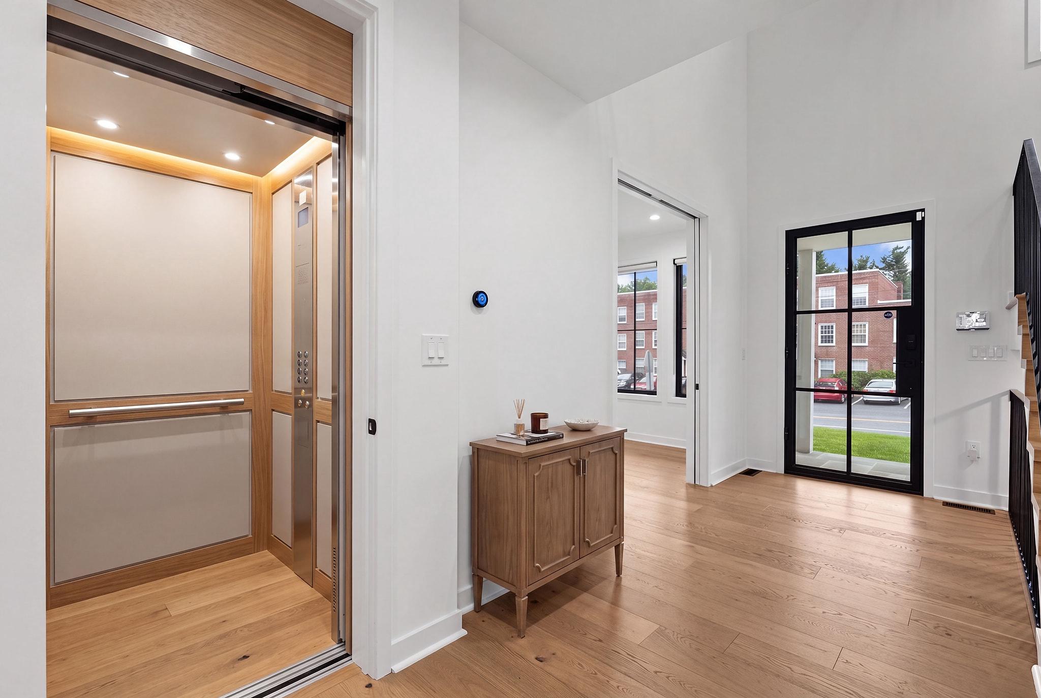 Home entry with a wood-paneled elevator, hardwood floors, and a black-framed glass front door.