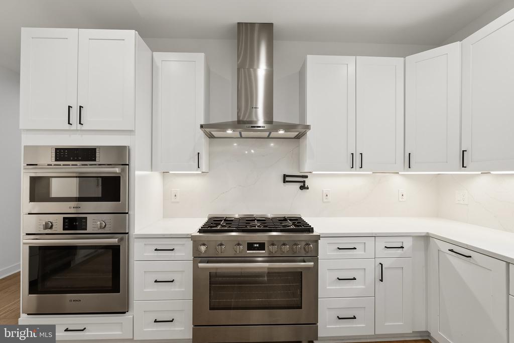White kitchen with stainless steel appliances, a large gas range, and a marble backsplash.