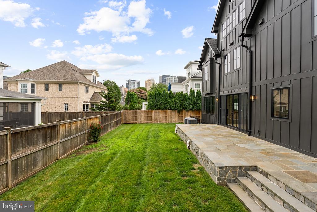 Rear of a dark-sided house beside a fenced lawn and stone patio.