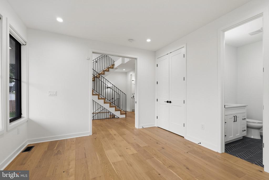 Empty room with light wood floors, a large window, and a view of the staircase.