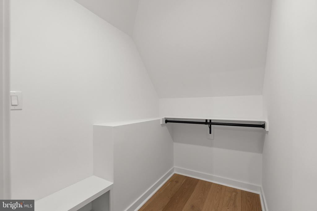 Empty walk-in closet with built-in shelves, a black hanging rod, and wood flooring.