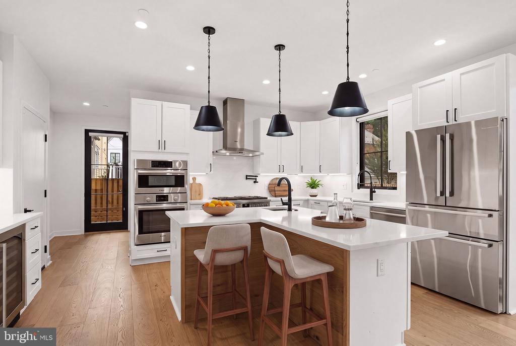 Bright white kitchen with stainless steel appliances and a large island with seating for two.