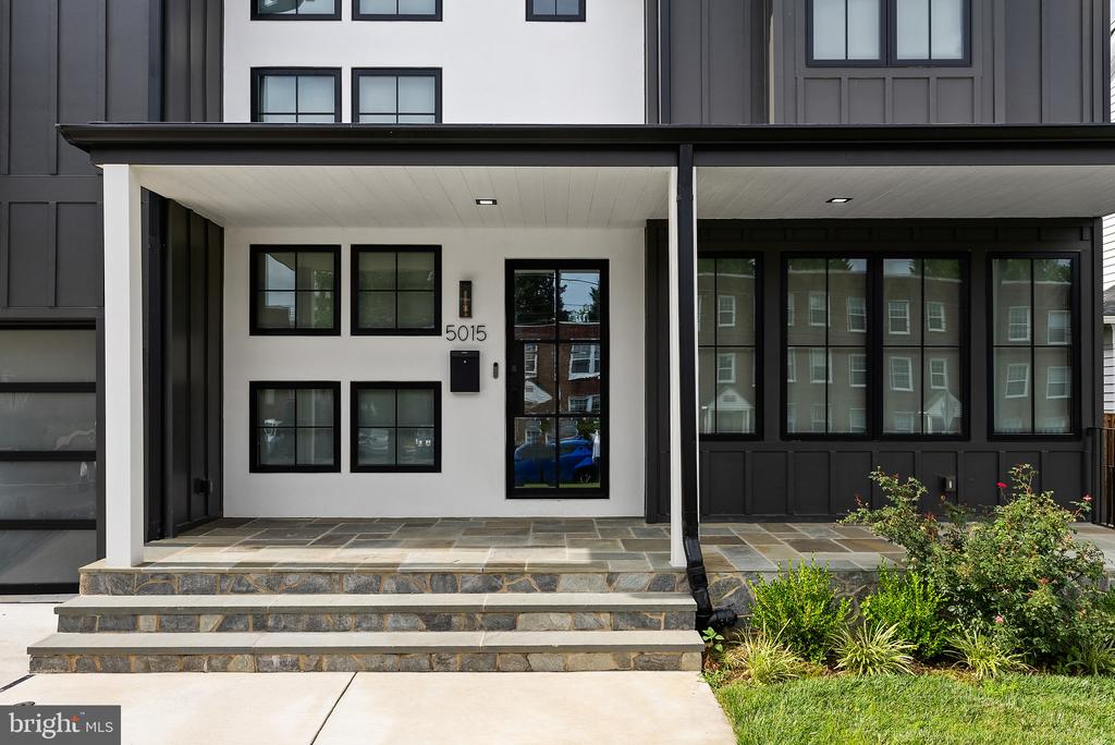 Modern home front entrance with covered porch, stone steps, and black-framed windows.