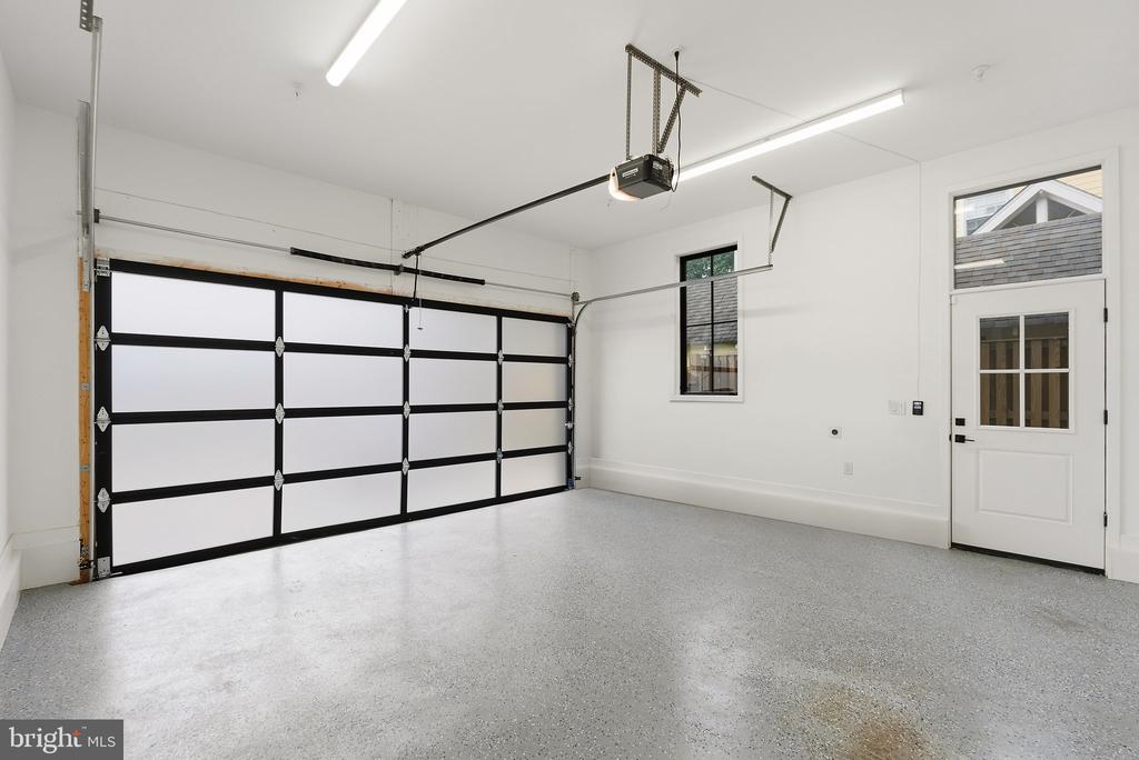 Empty garage with a speckled floor, black-and-white overhead door, and windowed side entrance.