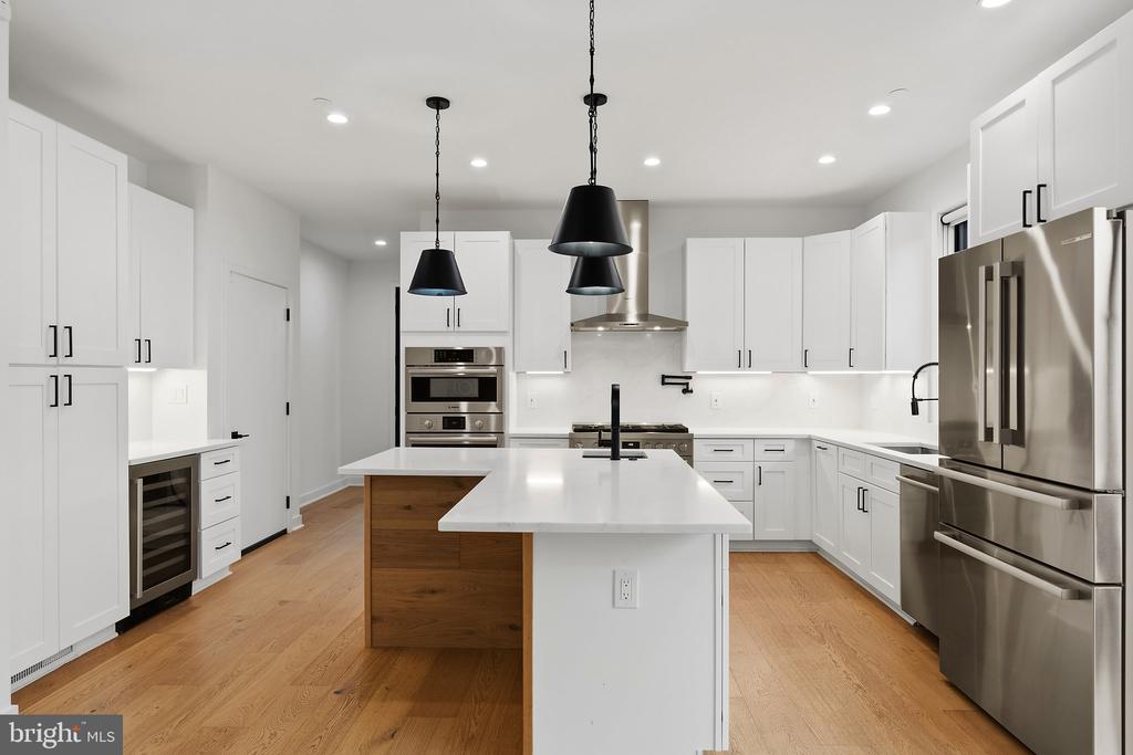 Modern kitchen with a large white island, white cabinetry, stainless steel appliances, and light hardwood floors.