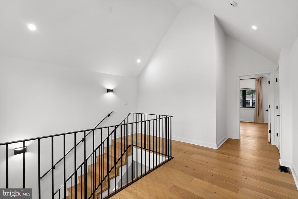 Upper-level landing with wood floors, black metal stair railing, and a tall vaulted ceiling.