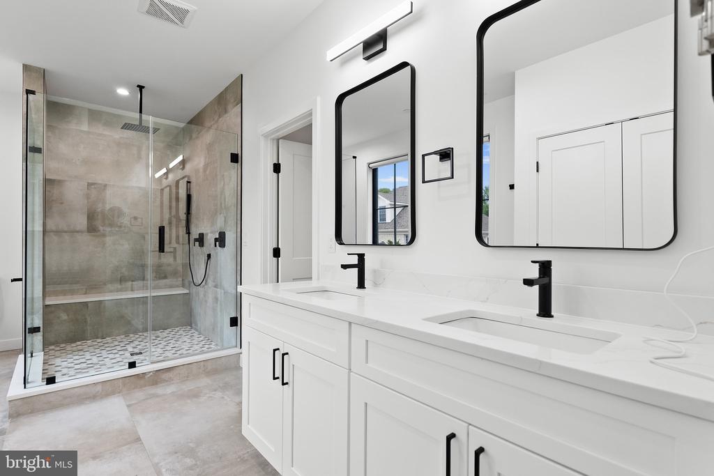 Renovated bathroom with a double vanity and glass-enclosed gray-tile shower.