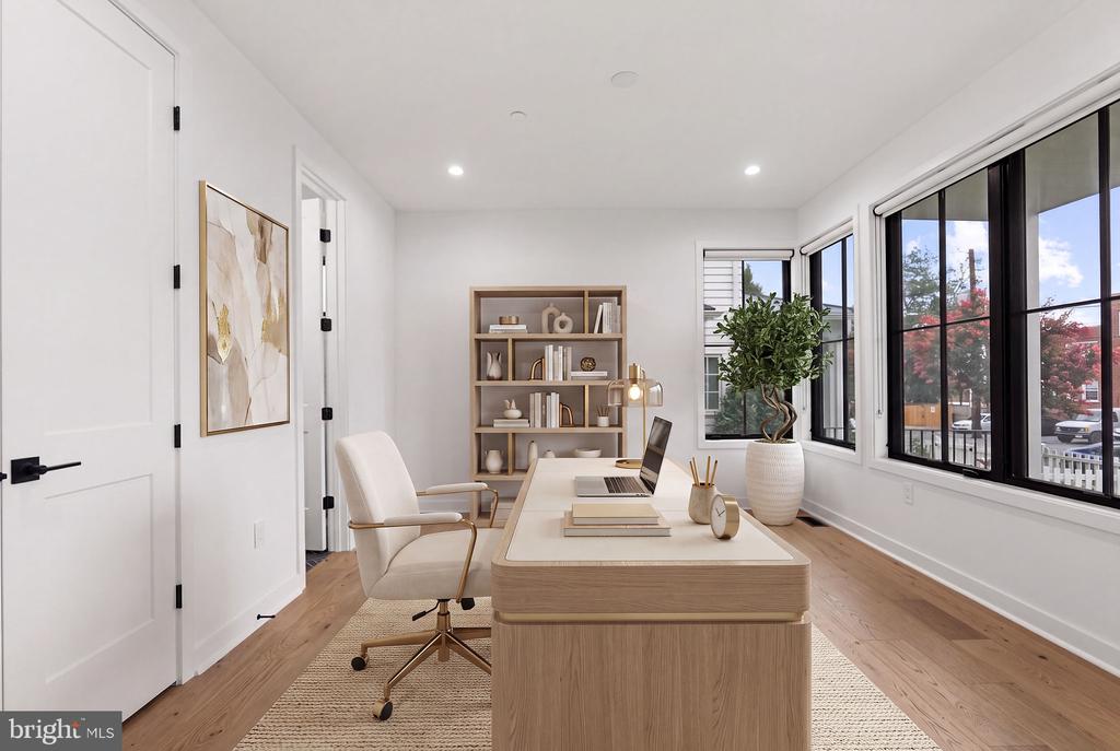 Staged home office with a light wood desk, built-in shelves, and large black-framed windows.