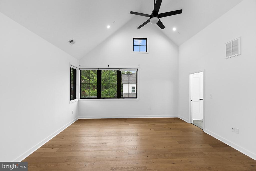 Empty vaulted room with light wood floors, a black ceiling fan, and large windows.