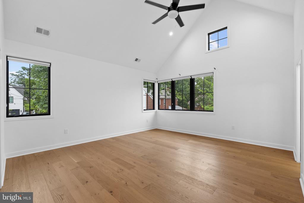 Empty vaulted room with hardwood floors, a ceiling fan, and black-framed windows.
