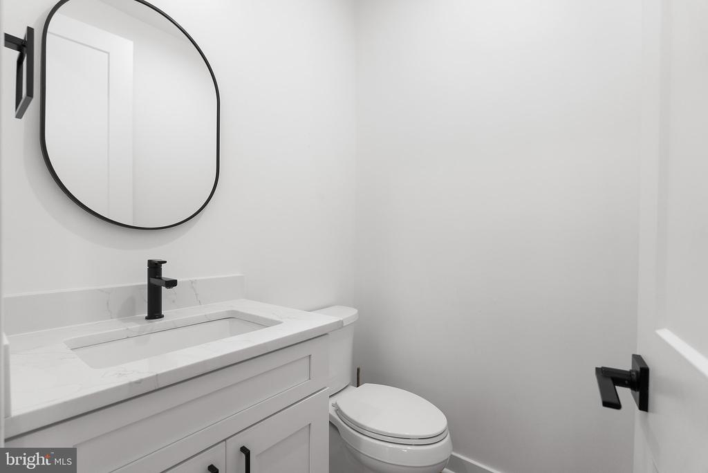 Modern bathroom with a white vanity, rounded mirror, black faucet, and toilet.