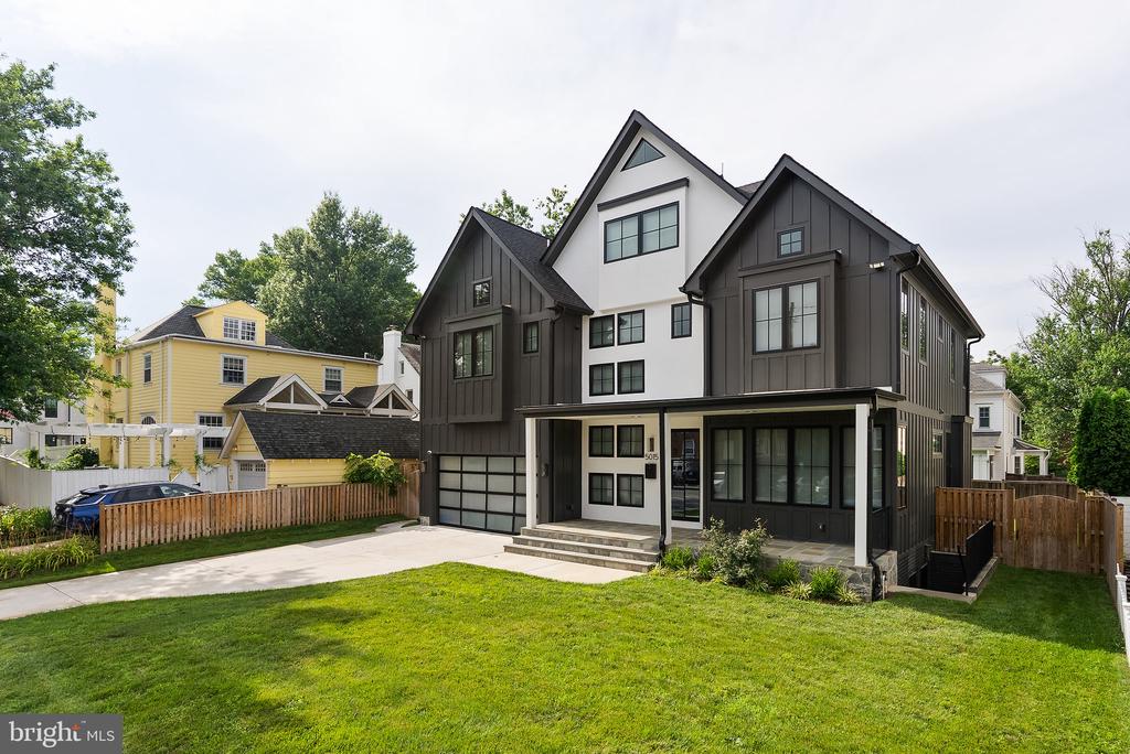 Modern multi-story home with dark siding, white facade, attached garage, and broad front lawn.