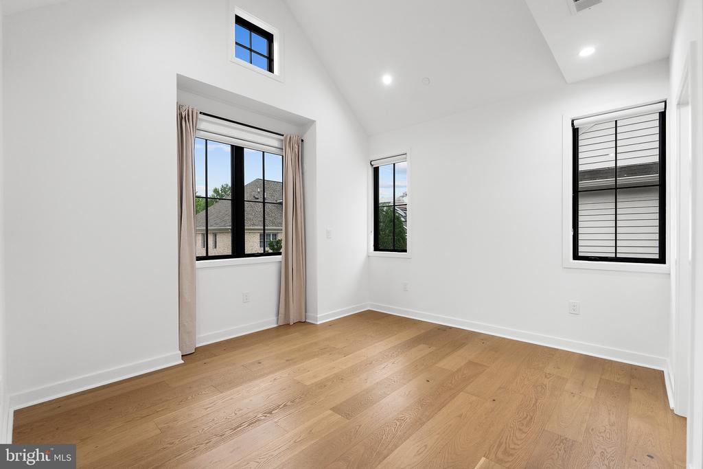 Empty room with light wood floors, a vaulted ceiling, and several black-framed windows.