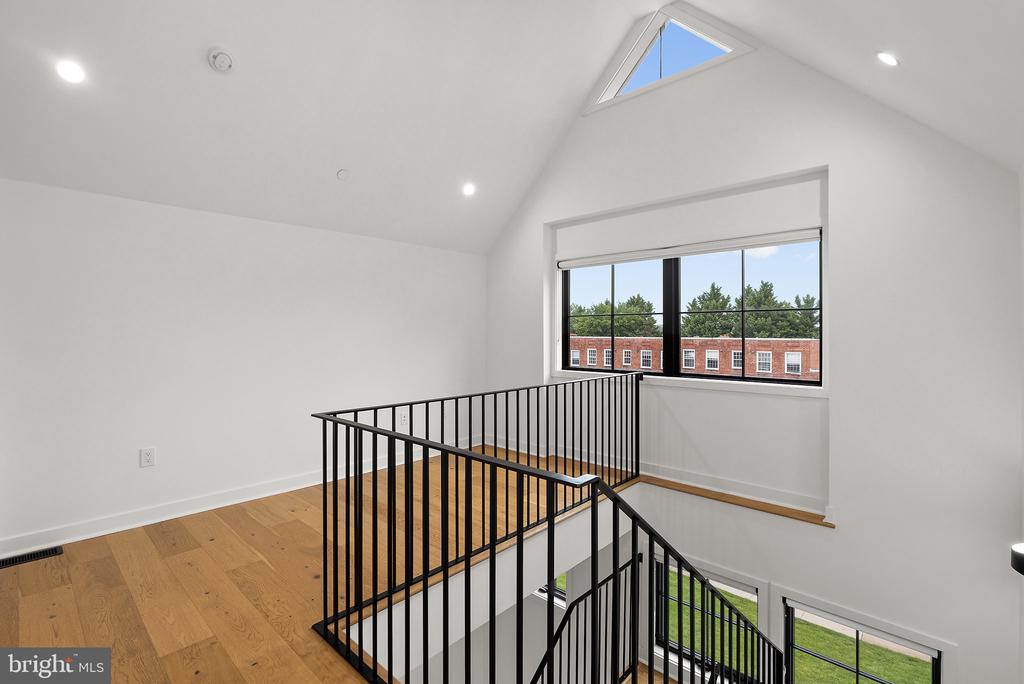 Upper-floor landing with wood floors, black stair railings, a skylight, and large windows.