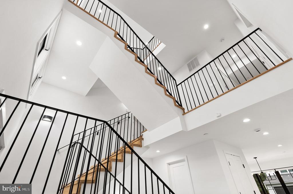 Multilevel stairwell with wood treads, black metal railings, and bright white walls.