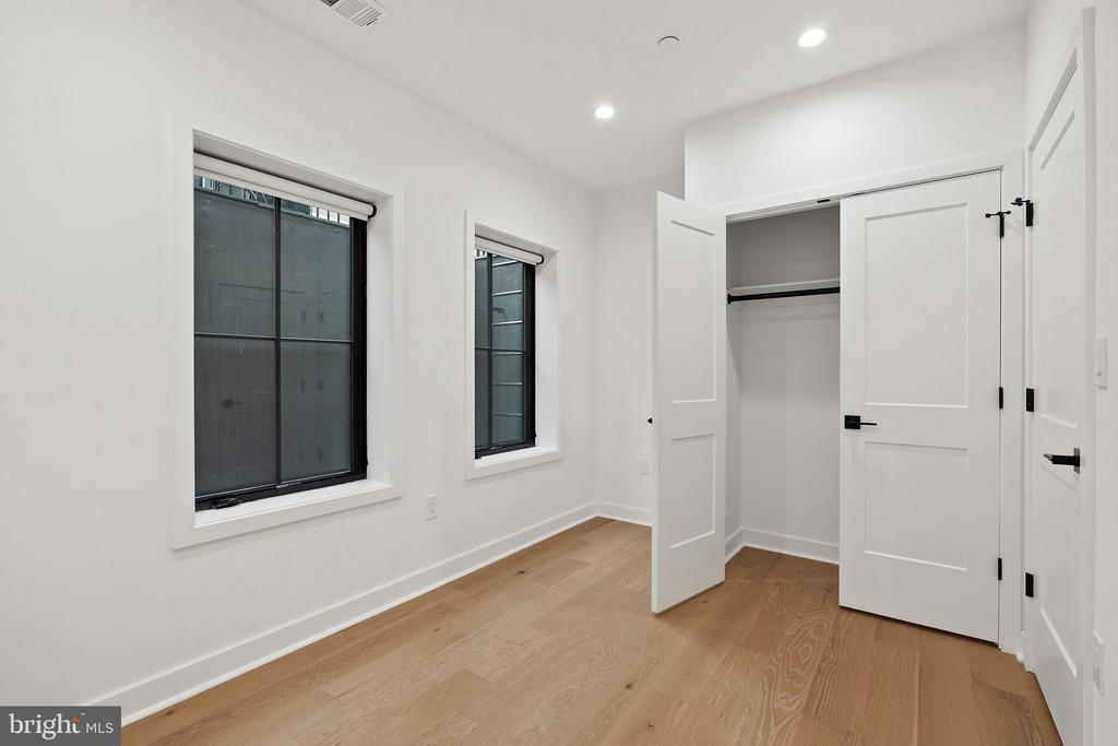 Vacant room with hardwood floors, two windows, and an open closet.