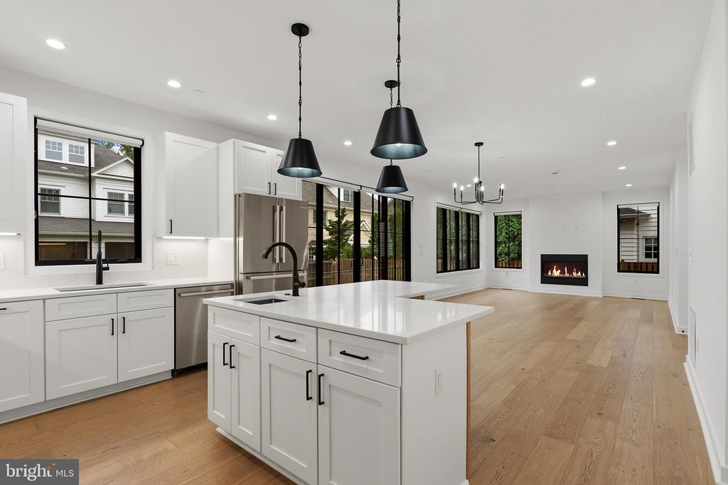 Modern white kitchen with a large island, stainless steel appliances, and an open living area with a fireplace.