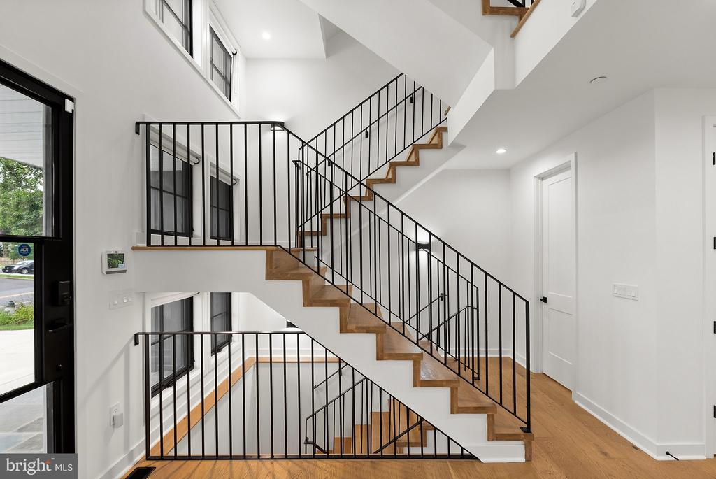 Two-story foyer with a switchback staircase, wood treads, black railings, and tall windows.