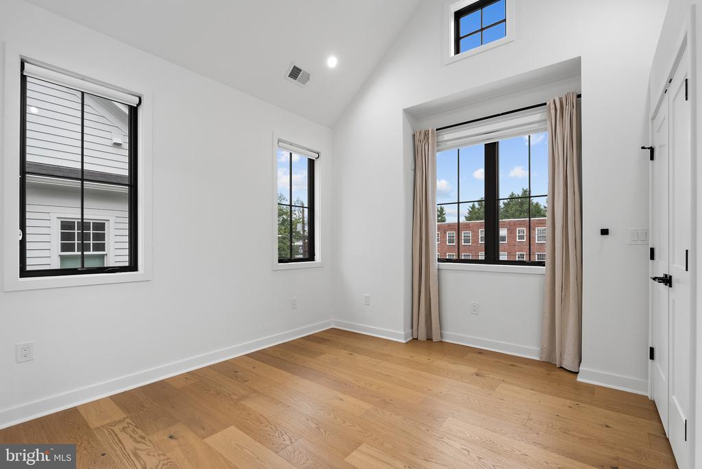 Empty room with hardwood floors, large black-framed windows, and beige curtains.