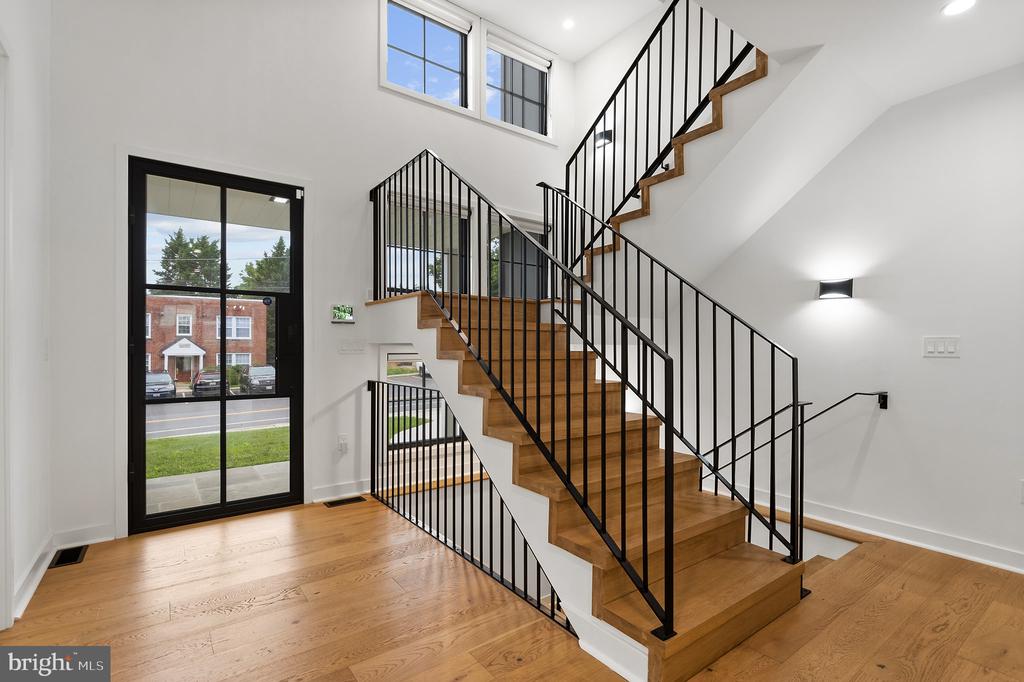 Entry hall with a multi-level wood staircase, black metal railings, hardwood floors, and tall windows.