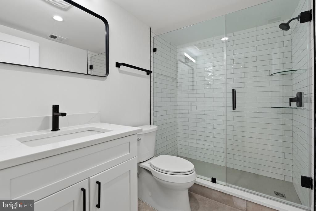 Modern bathroom with a white vanity, black fixtures, and a glass-enclosed subway-tile shower.